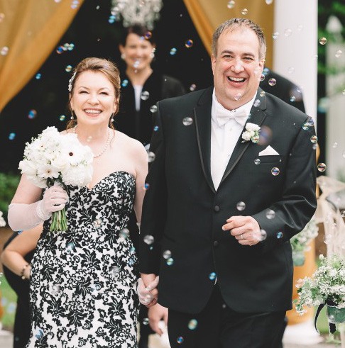 Love U success story of bride wearing a black lace dress holding white flowers with her groom